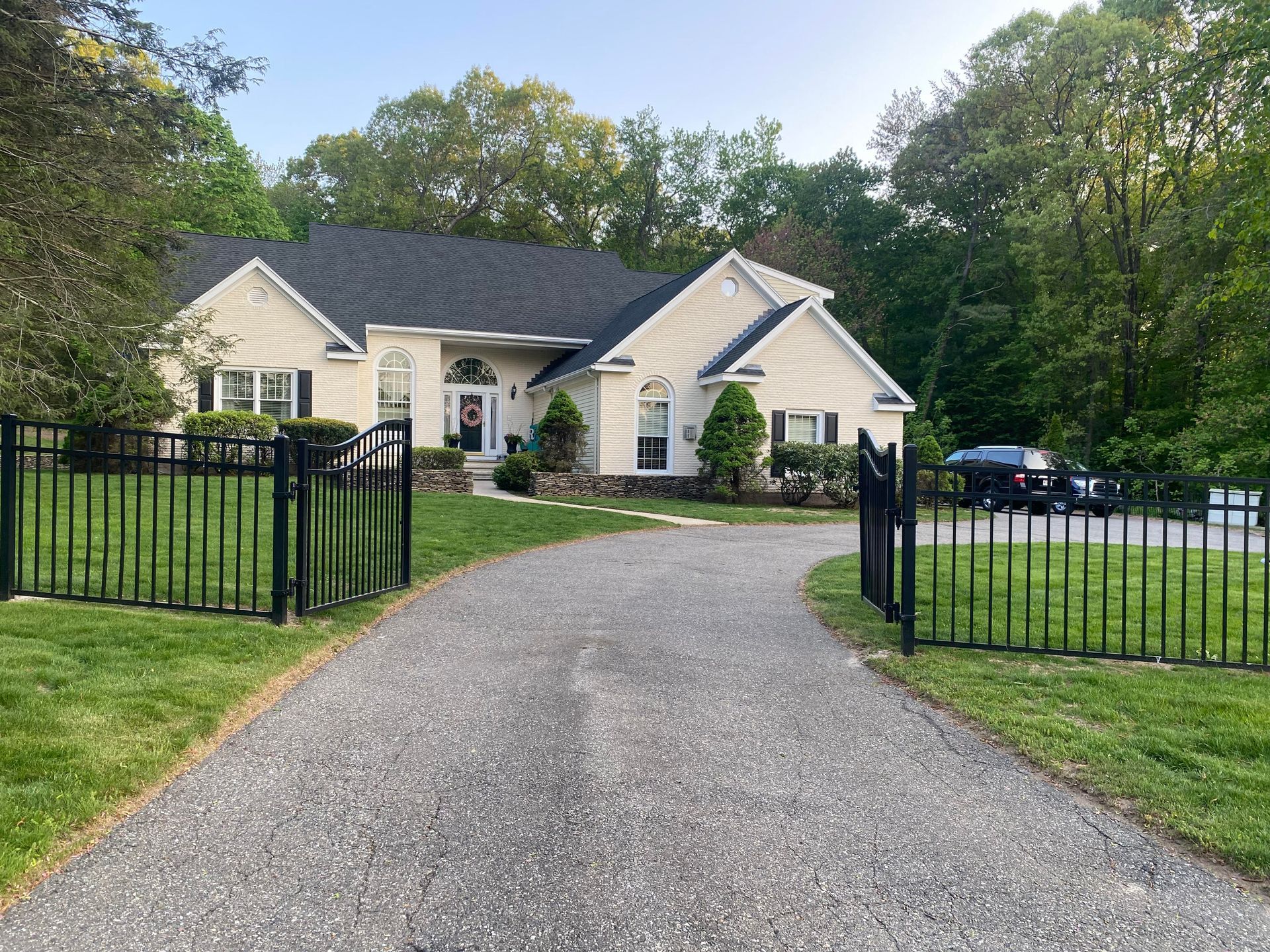 A large white house with a black fence and a gravel driveway leading to it.