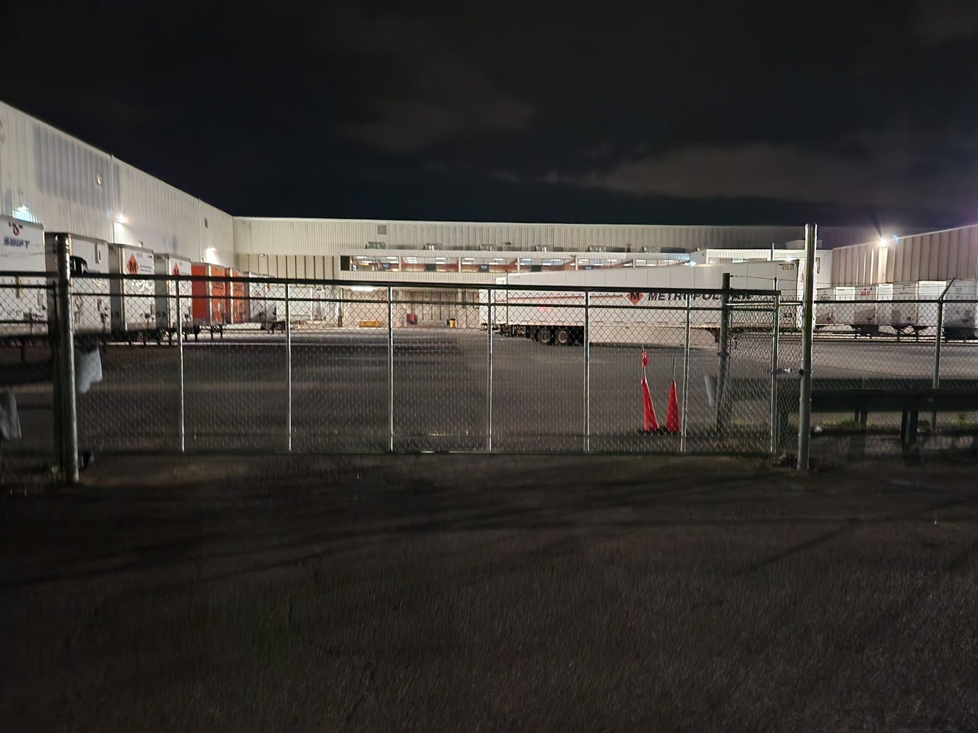 A fence is surrounding a large warehouse at night.