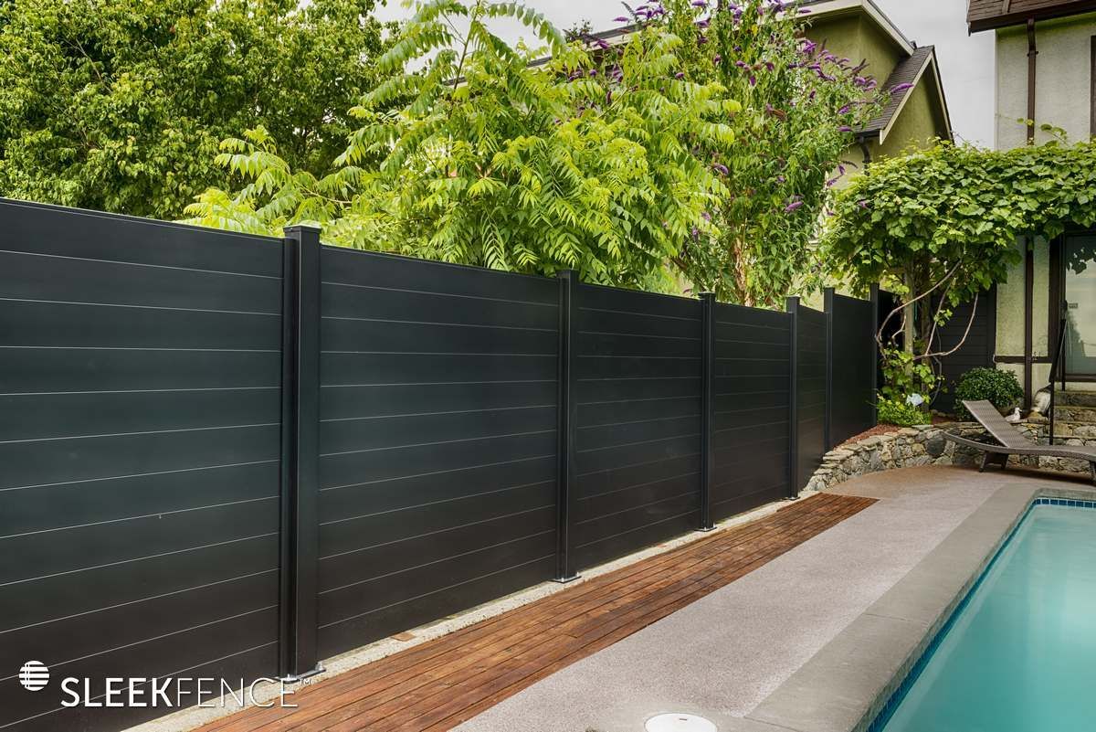 A black fence surrounds a swimming pool in a backyard.