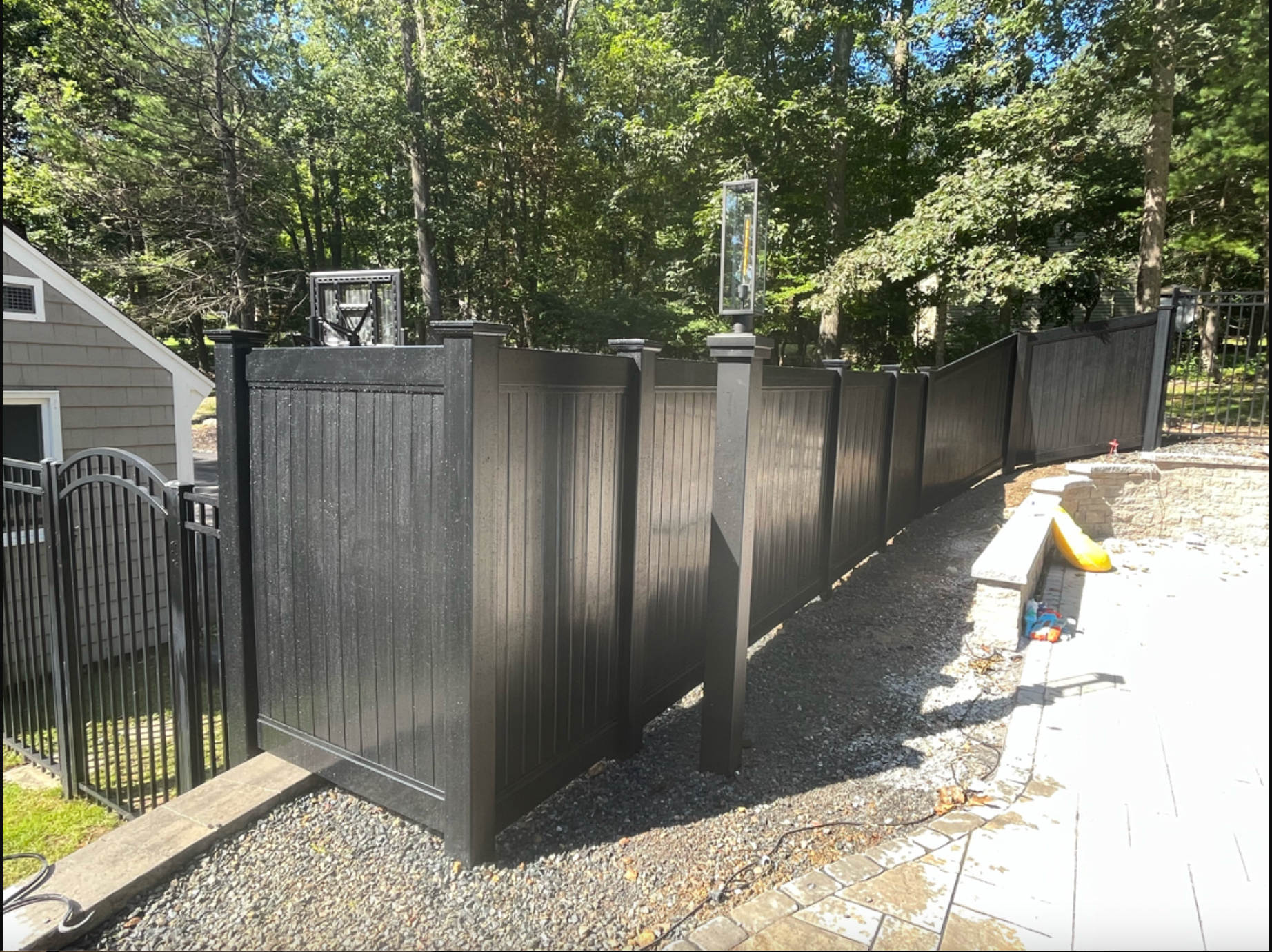 A black fence is surrounded by trees and gravel in front of a house.