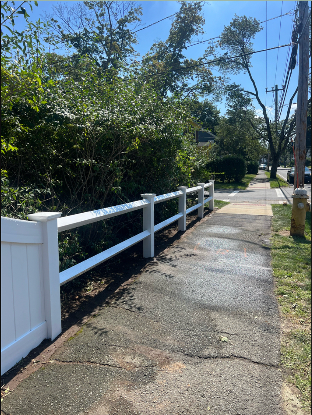 A white fence along a sidewalk next to a road.