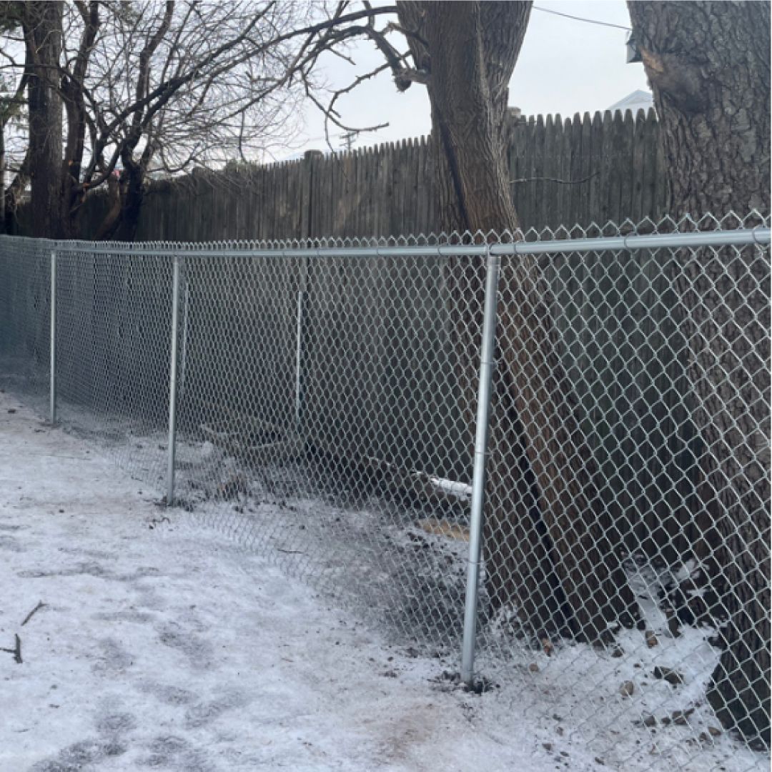 A chain link fence is surrounded by snow and trees.