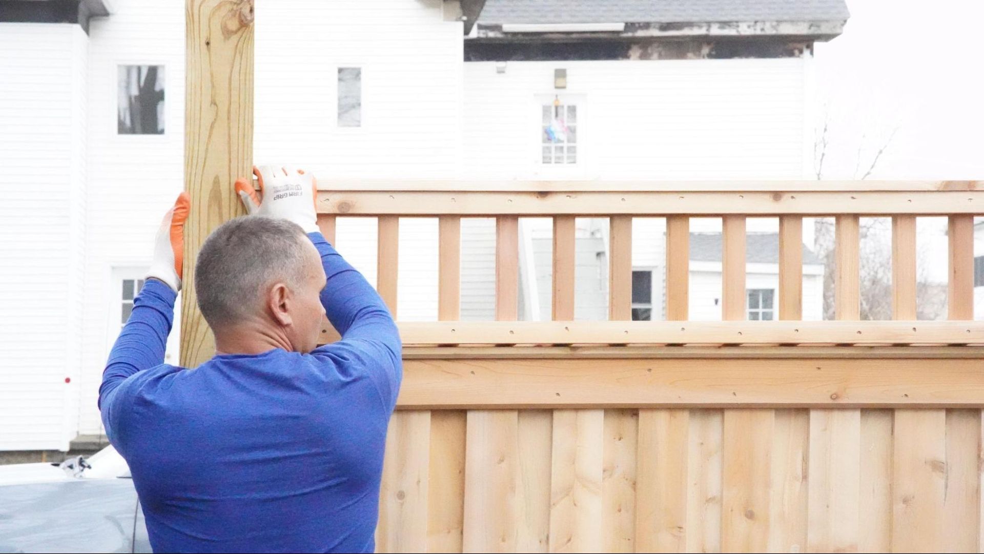 A man in a blue shirt is installing a wooden fence in Beverly, MA from a top fencing company in the North Shore Patriot Fence