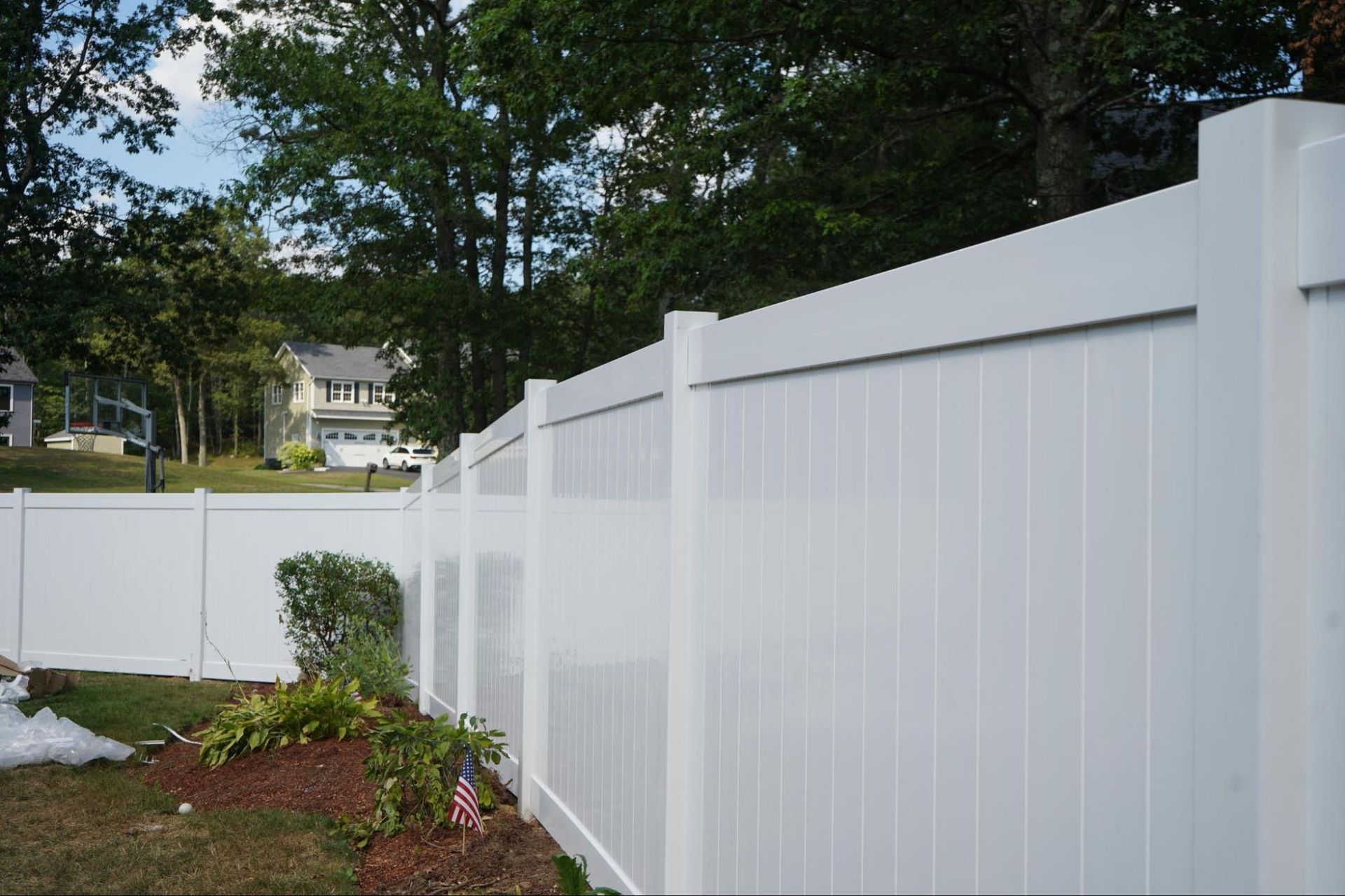 White vinyl fence bordering a yard with trees and houses in the background.