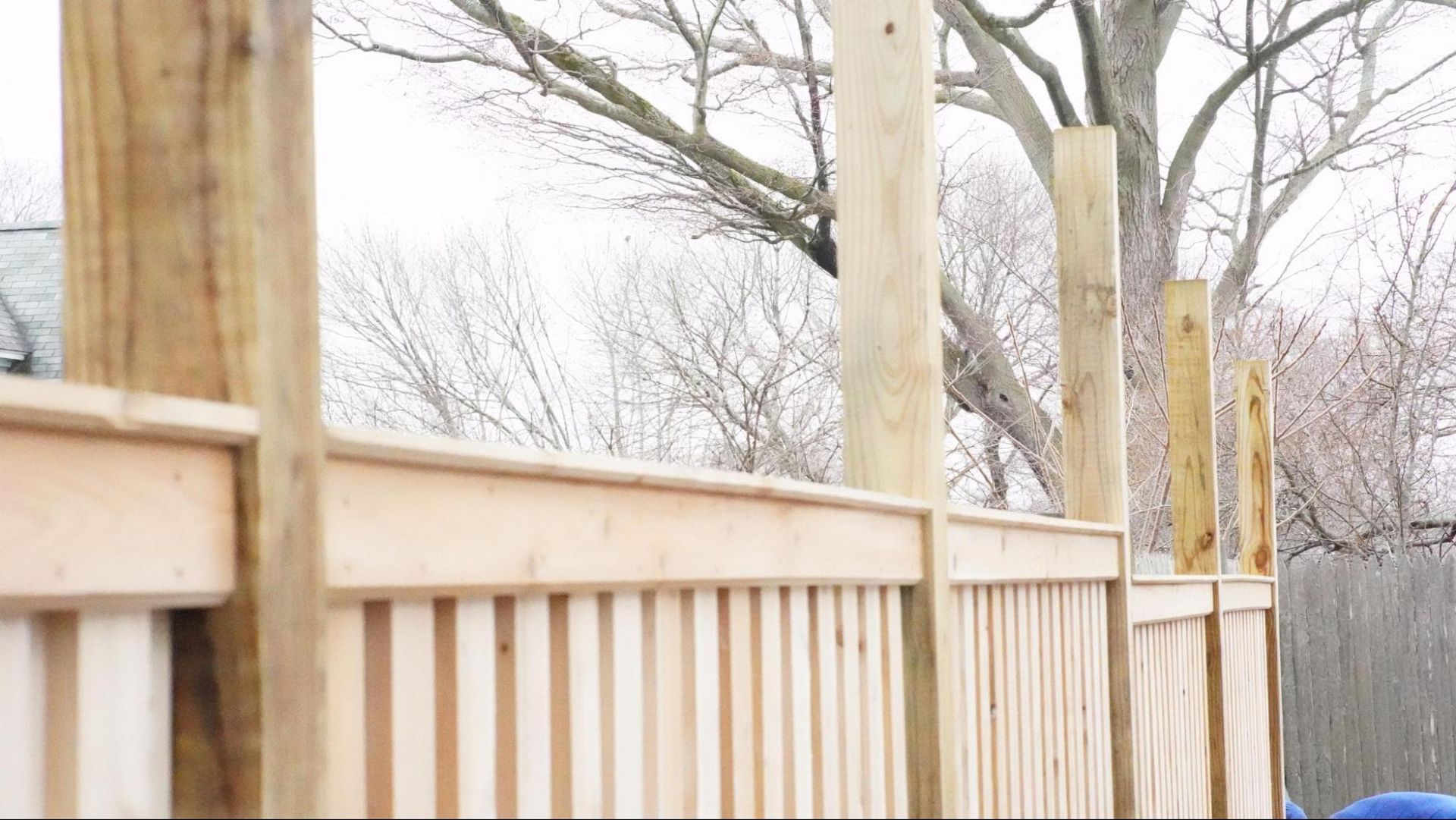 A wooden fence under construction, featuring vertical posts and horizontal slats in a backyard setting.