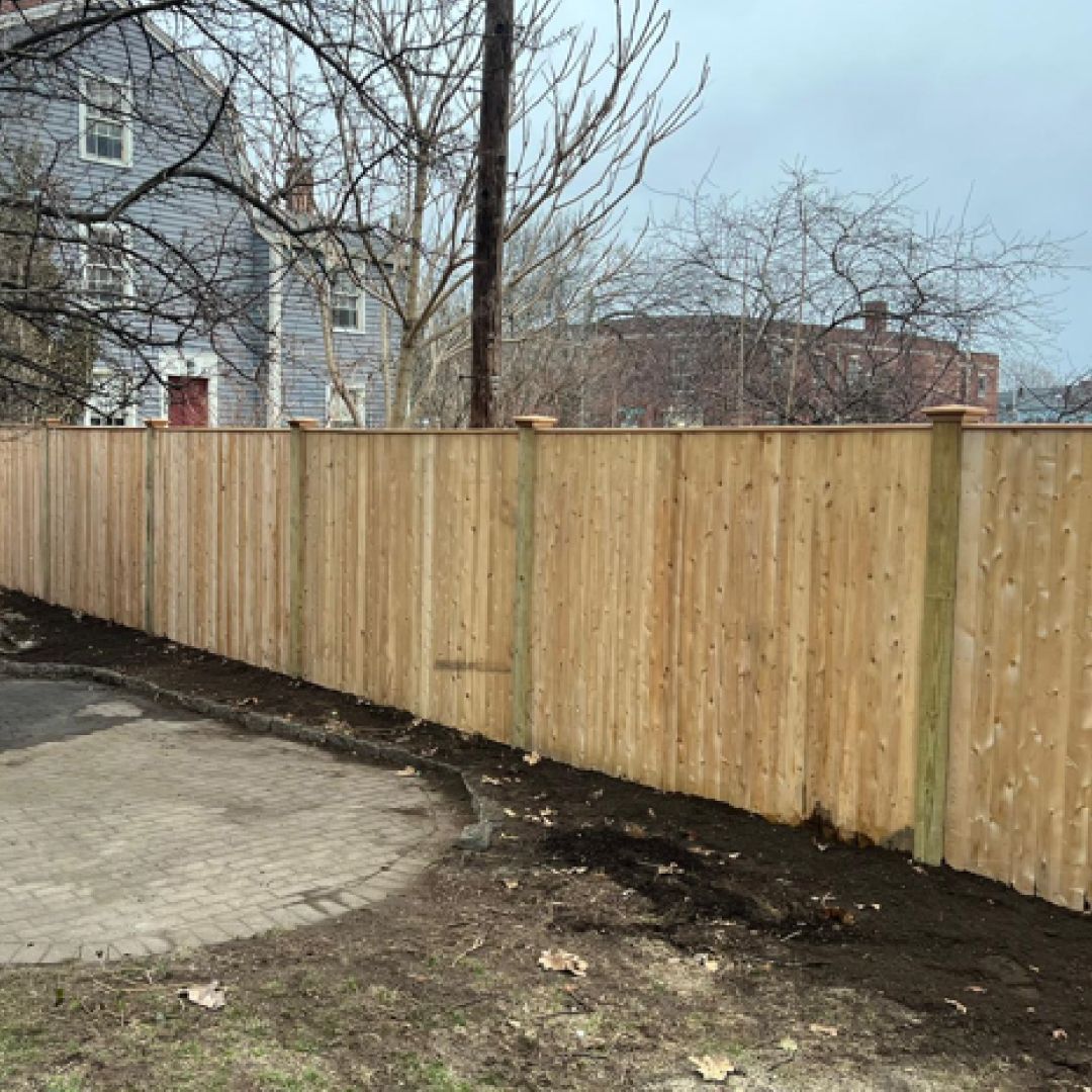 A wooden fence is sitting next to a dirt road in front of a house.