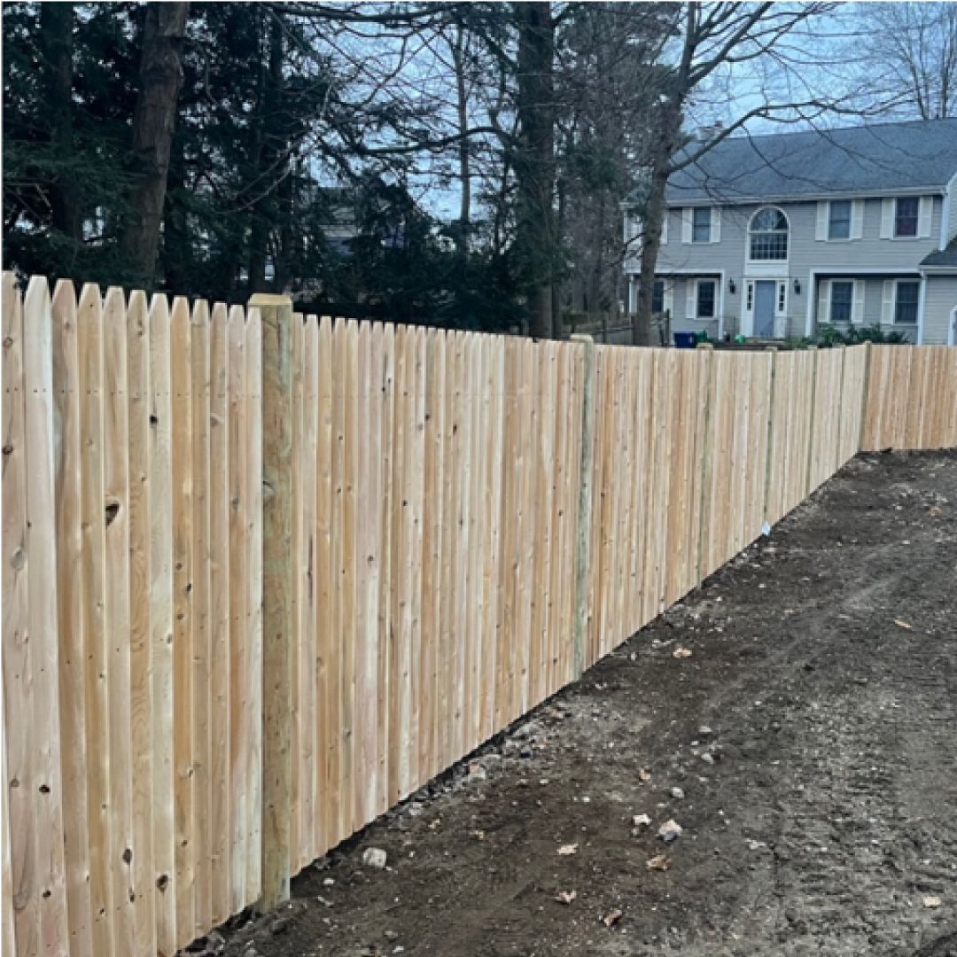 A wooden fence is surrounding a dirt field in front of a house.