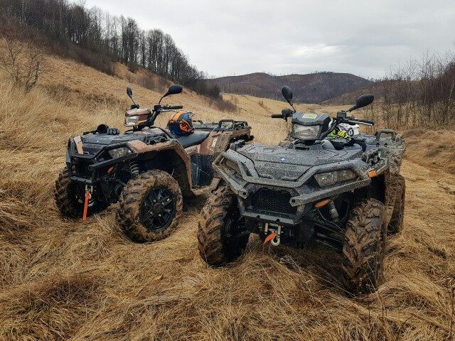Two muddy ATVs parked on a grassy hillside.