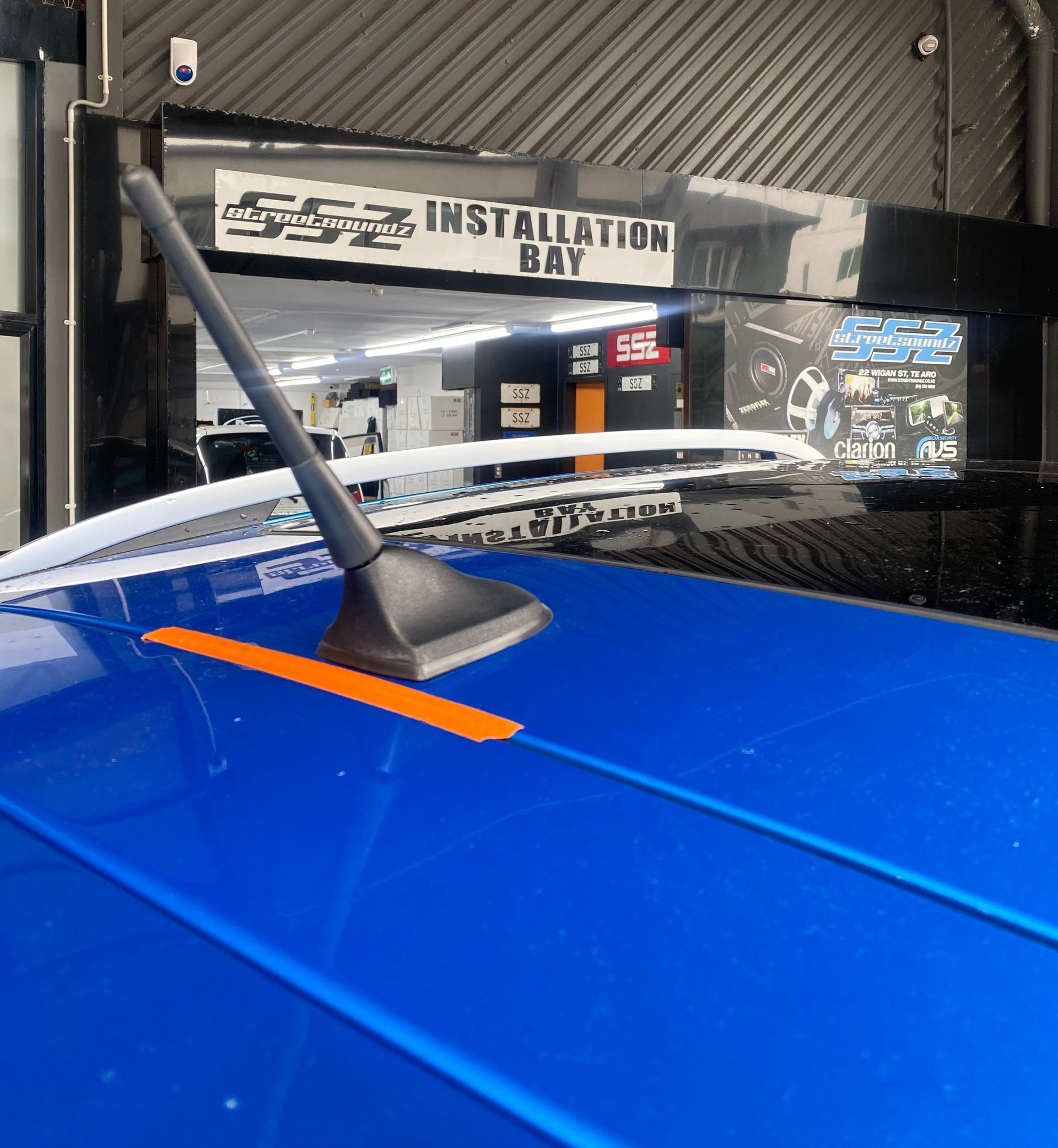 Blue car roof with black antenna and orange stripe, Installation Bay in background.