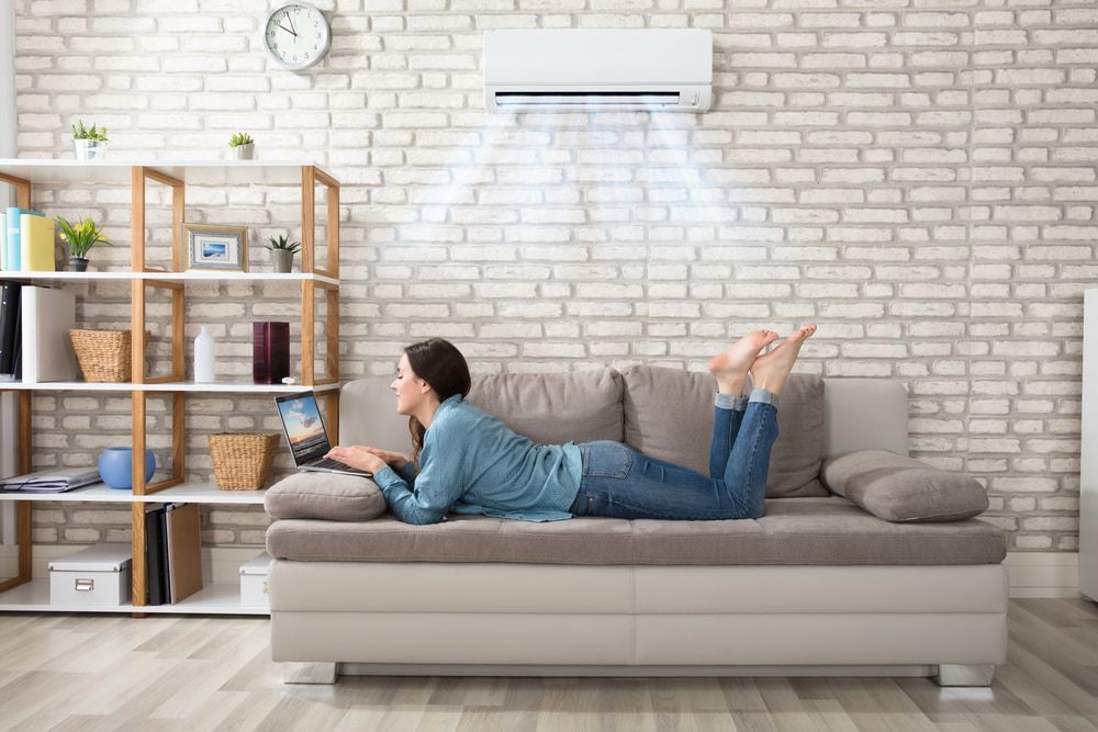 Woman Lying On Sofa Enjoying The Cooling Of Air Conditioner — Oriel Refrigeration and Air Conditioning in Peak Hill, NSW
