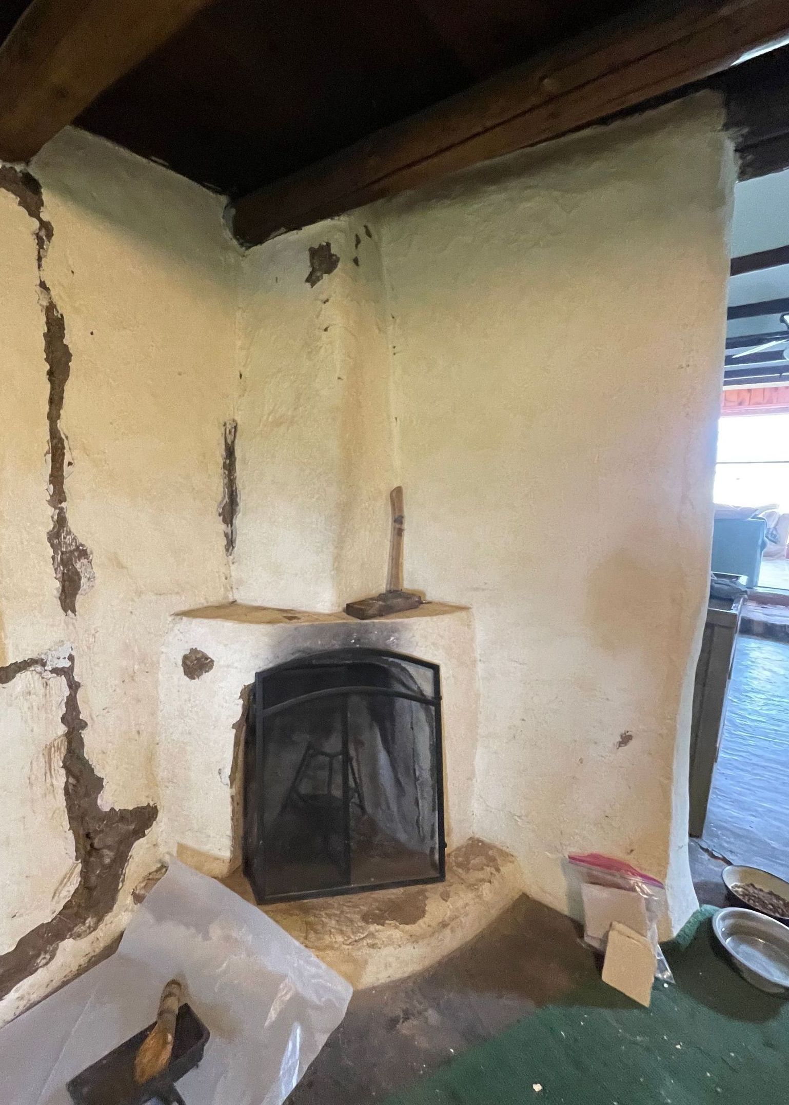 An old adobe fireplace with white plaster peeling off and large holes in the mud