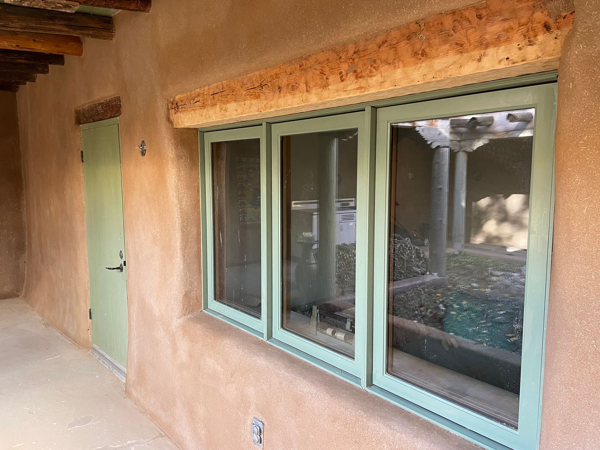 Exterior window with green trim and beautiful adobe plaster.