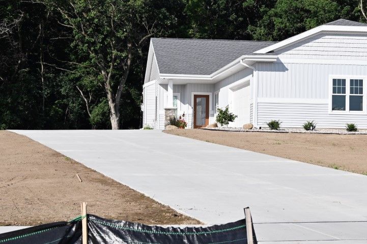 White house with gray roof and long concrete driveway beside a brown yard and trees