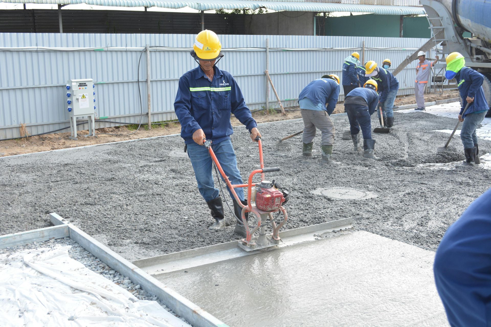 Workers in hard hats smoothing wet concrete with a power trowel at a construction site