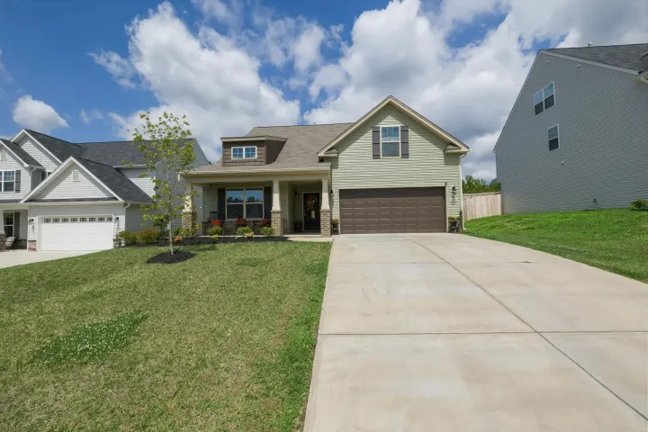 Suburban house with a front porch, garage, and long concrete driveway under a partly cloudy sky