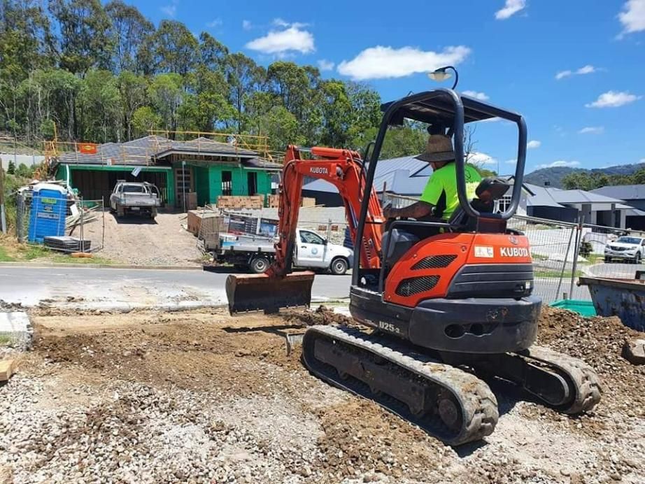 A Man Is Driving a Small Excavator on A Construction Site — Kontek Constructions in Brisbane, QLD