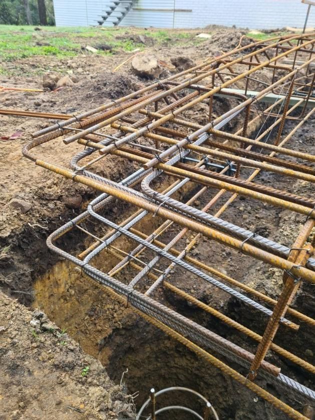 A Bunch of Metal Bars Are Sitting on Top of Each Other in The Dirt — Kontek Constructions in Beaudesert, QLD