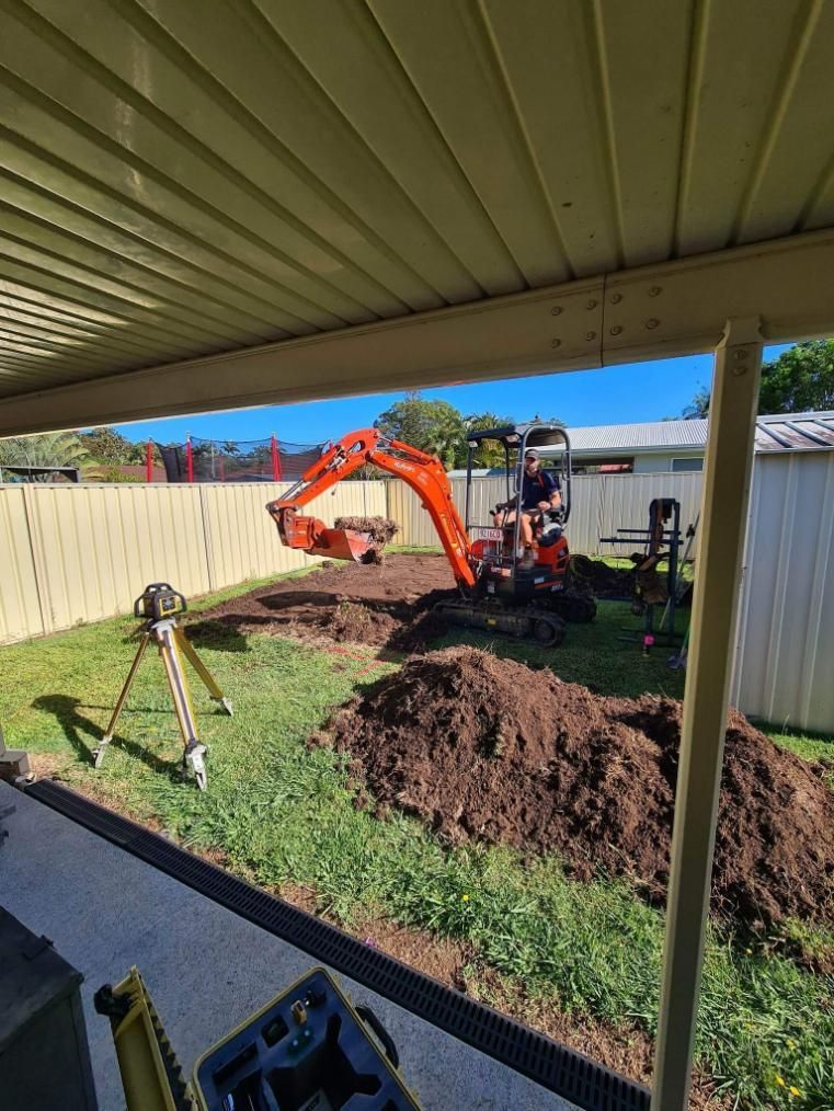 A Small Excavator Is Digging a Hole in A Backyard — Kontek Constructions in Brisbane, QLD