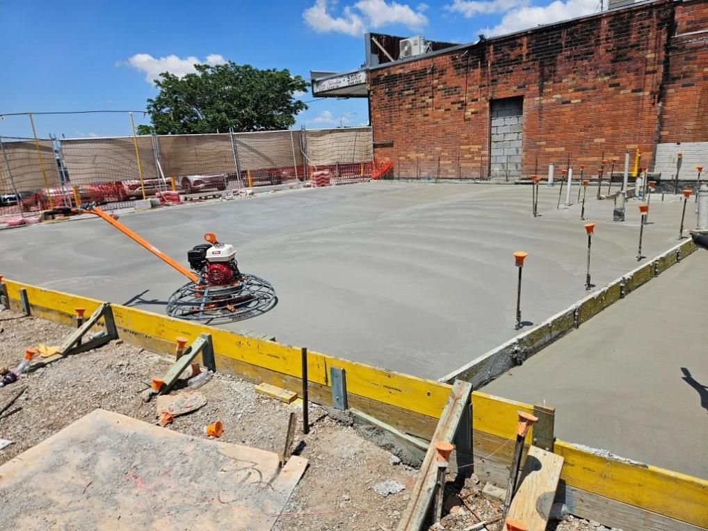 A Concrete Floor Is Being Built in Front of A Brick Building — Kontek Constructions in Jimboomba, QLD