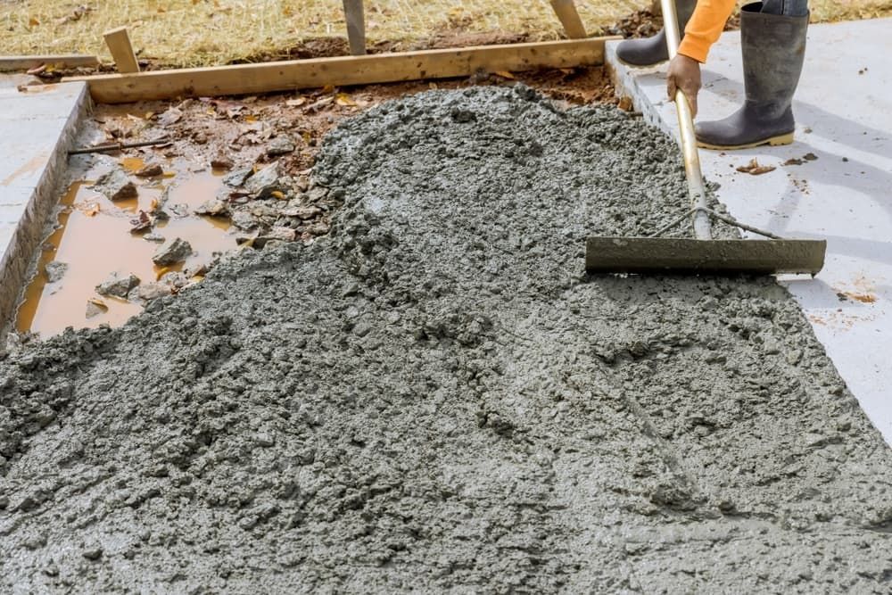 A Man is Spreading Concrete on a Sidewalk With a Rake — Kontek Constructions in Jimboomba, QLD