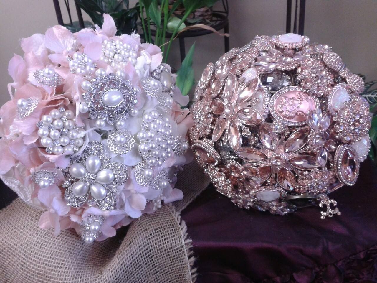 Two ornate beaded floral brooches, one pink and one rose gold, resting on fabric