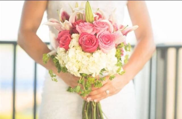 Bride holding a bouquet of pink roses, white flowers, and greenery in a bright indoor setting