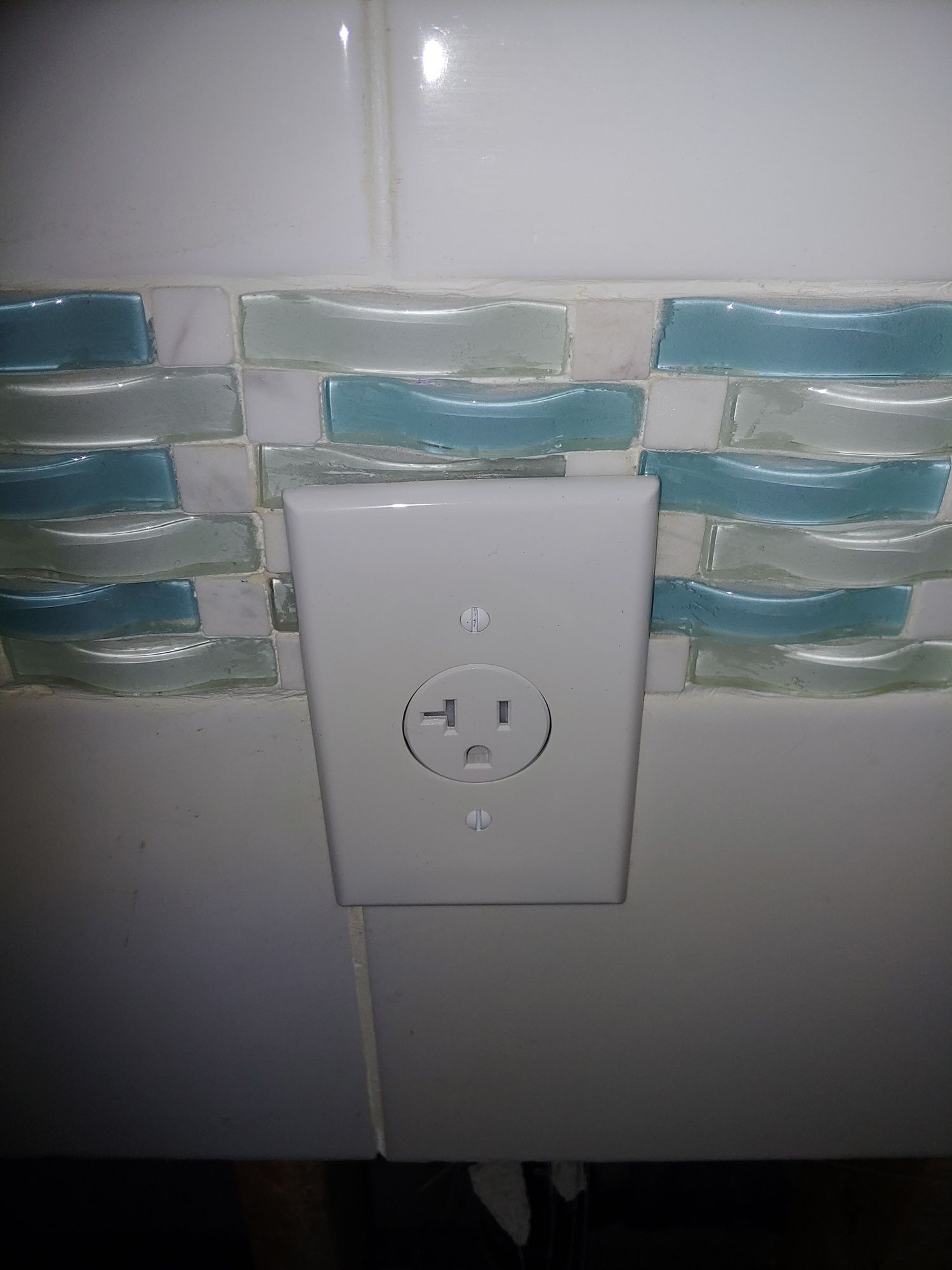 A white electrical outlet is sitting on a tiled wall.