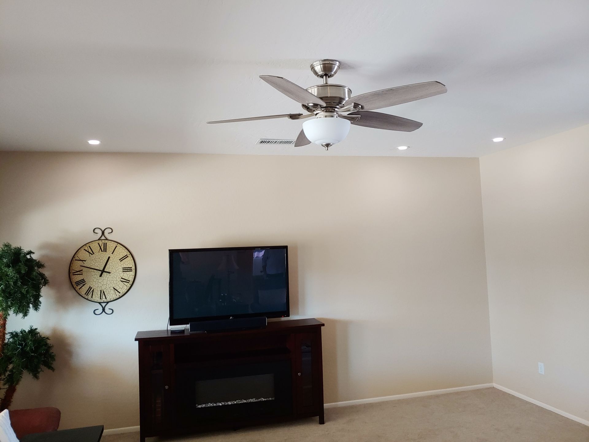 A living room with a fireplace , television , clock and ceiling fan.