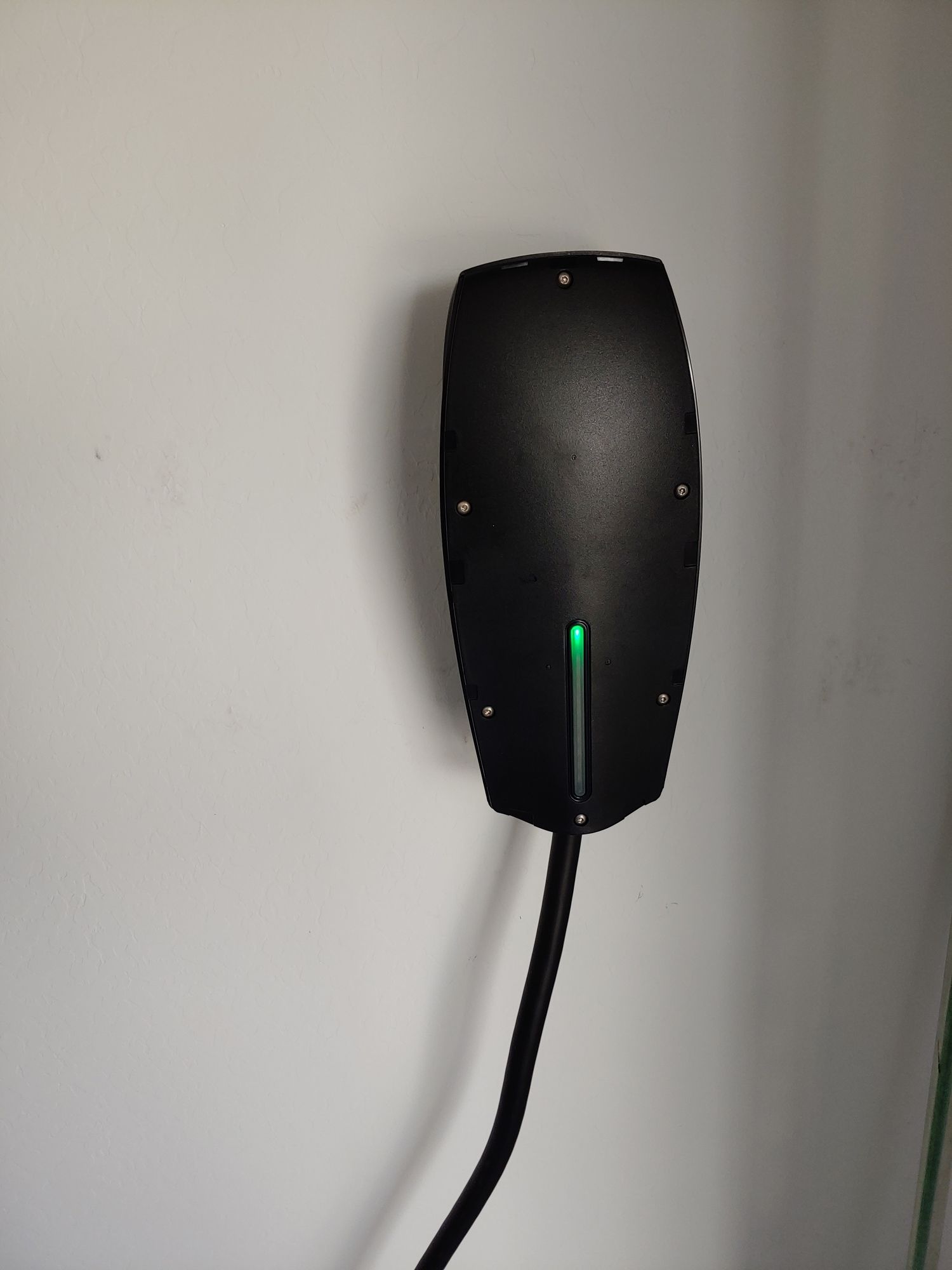 A black device with a green light on it is plugged into a wall.