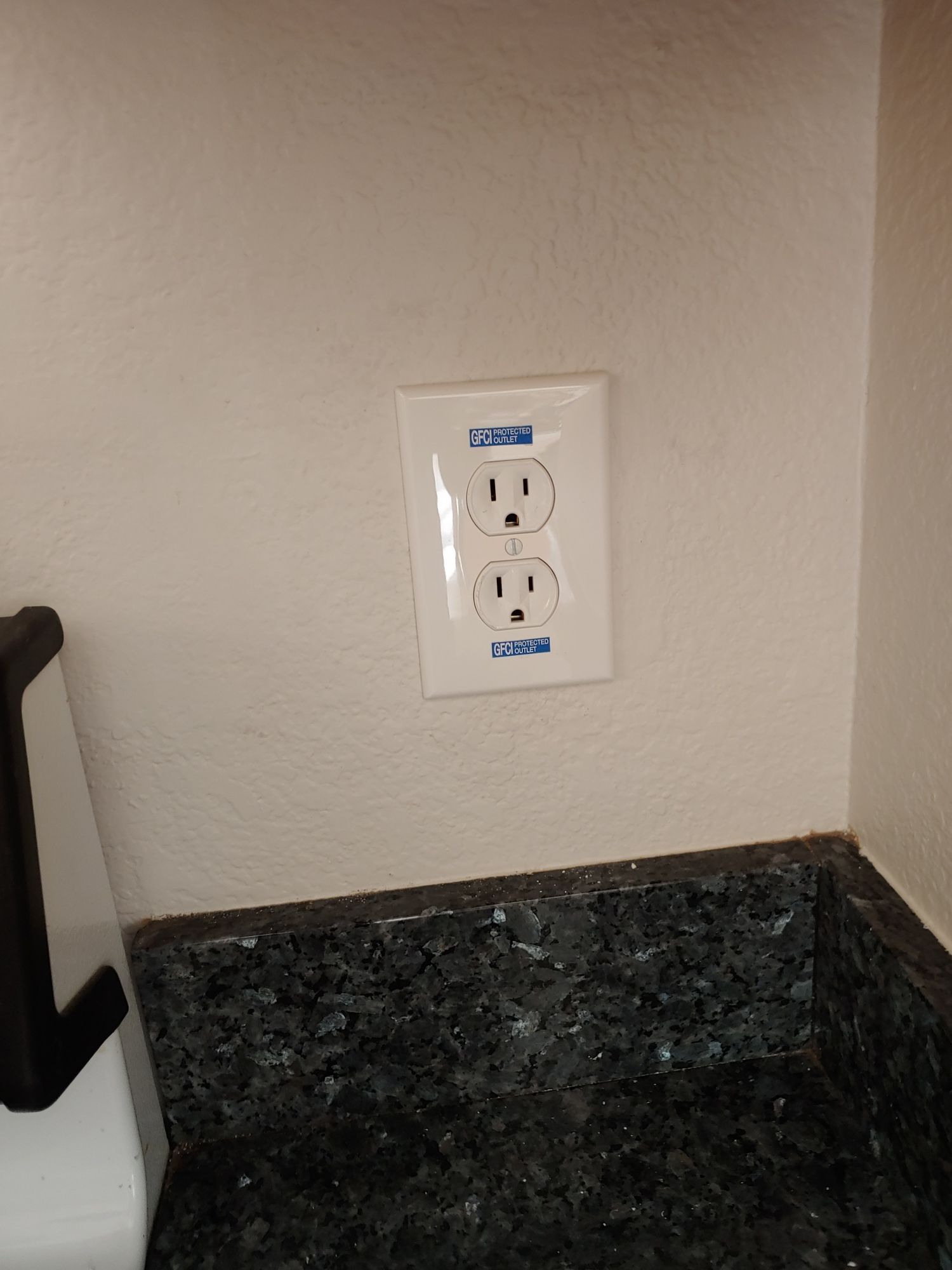 There is a double electrical outlet on the wall next to a counter.