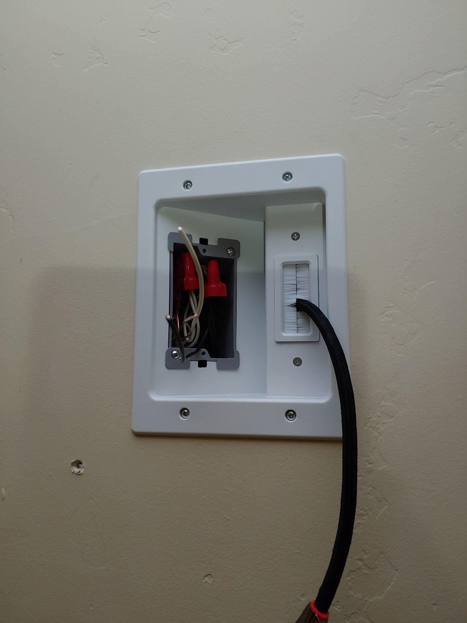 A black cord is plugged into a white box on a wall