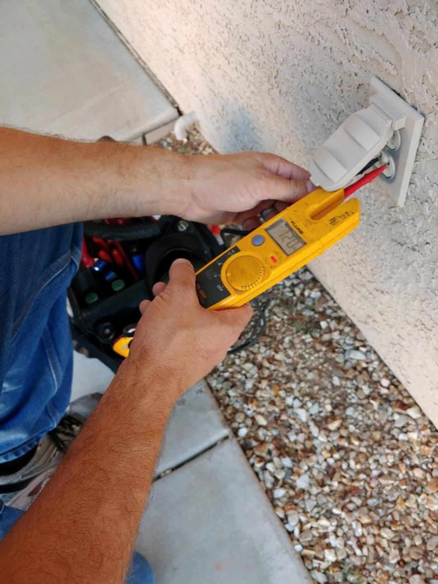 A man is using a clamp meter to test an electrical outlet.