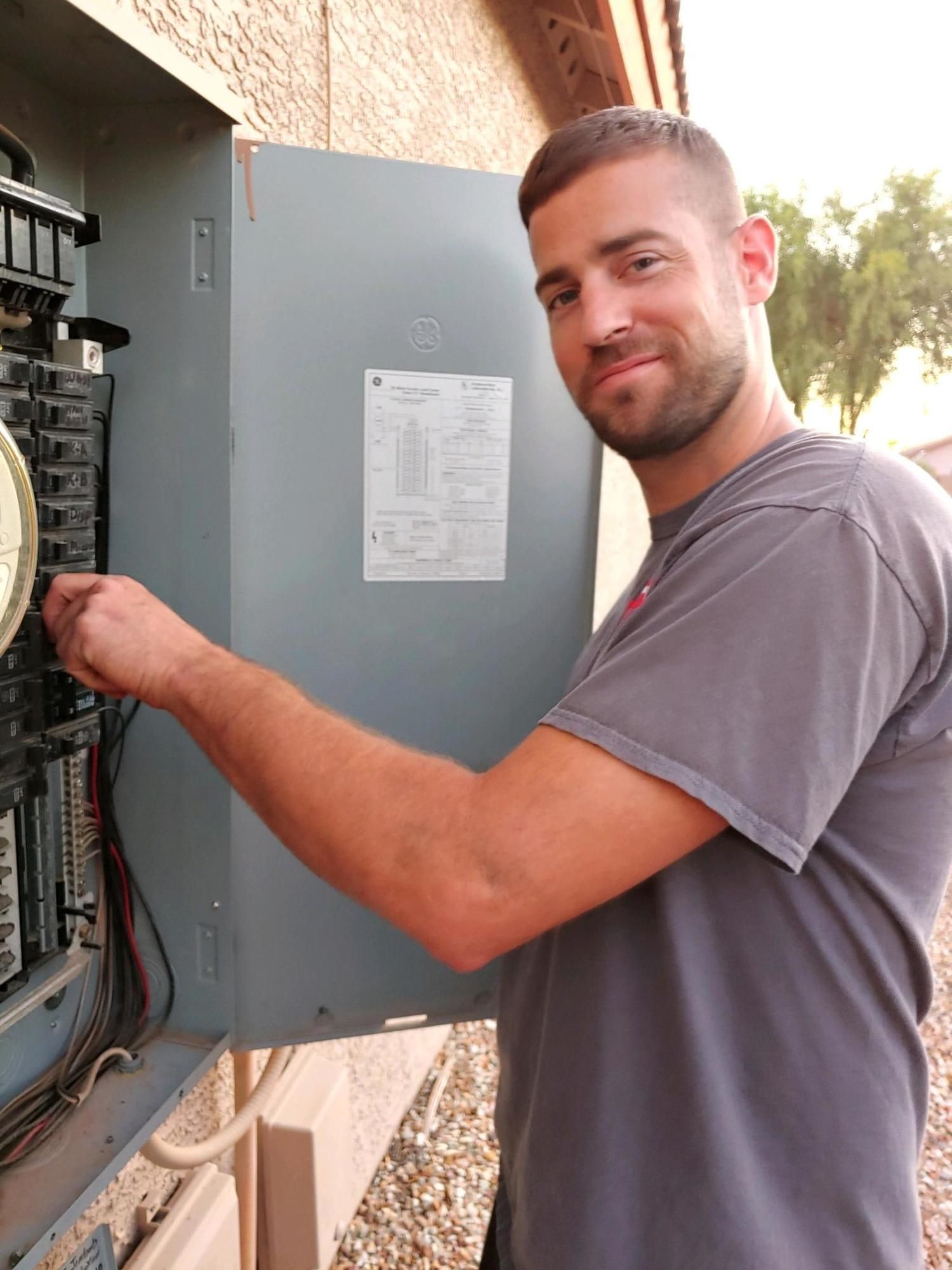 A man in a gray shirt is working on an electrical box