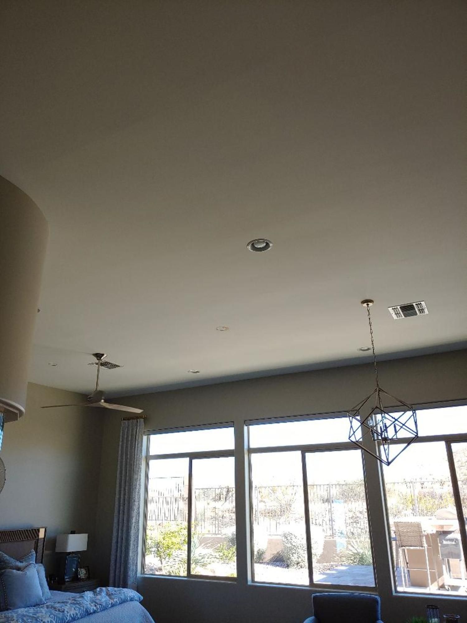 A bedroom with a bed , ceiling fan , and lots of windows.