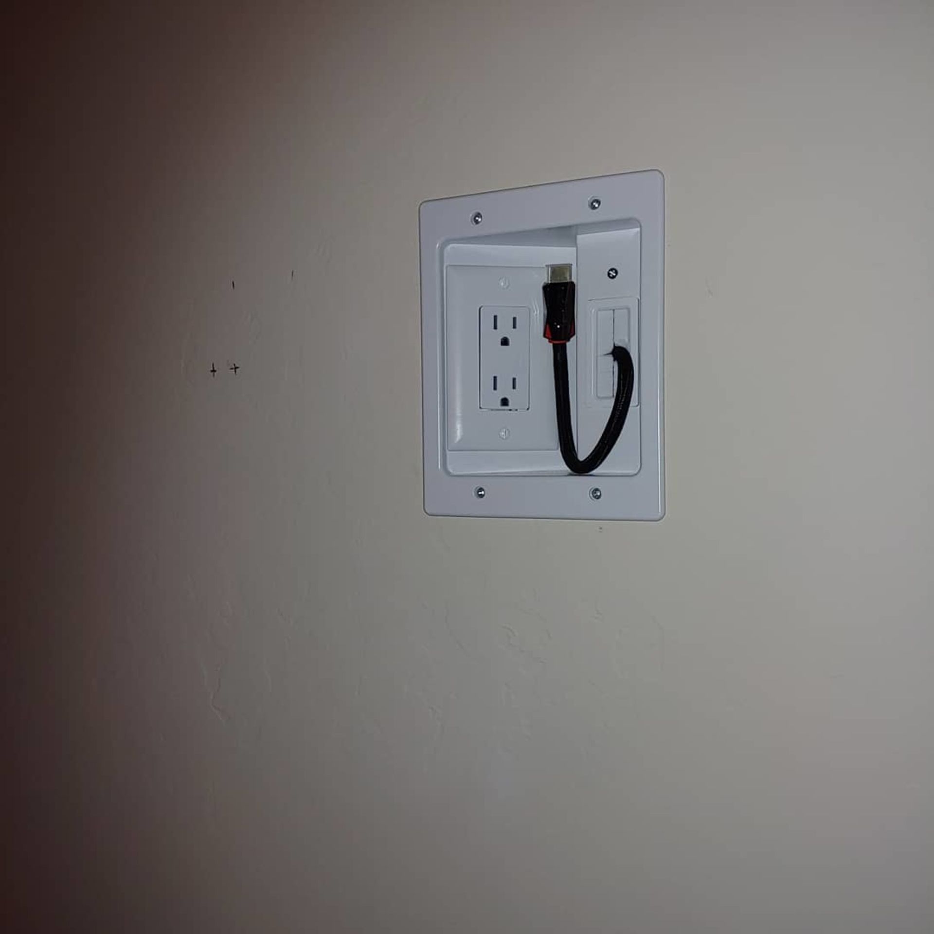 A white electrical outlet with a black cord plugged into it