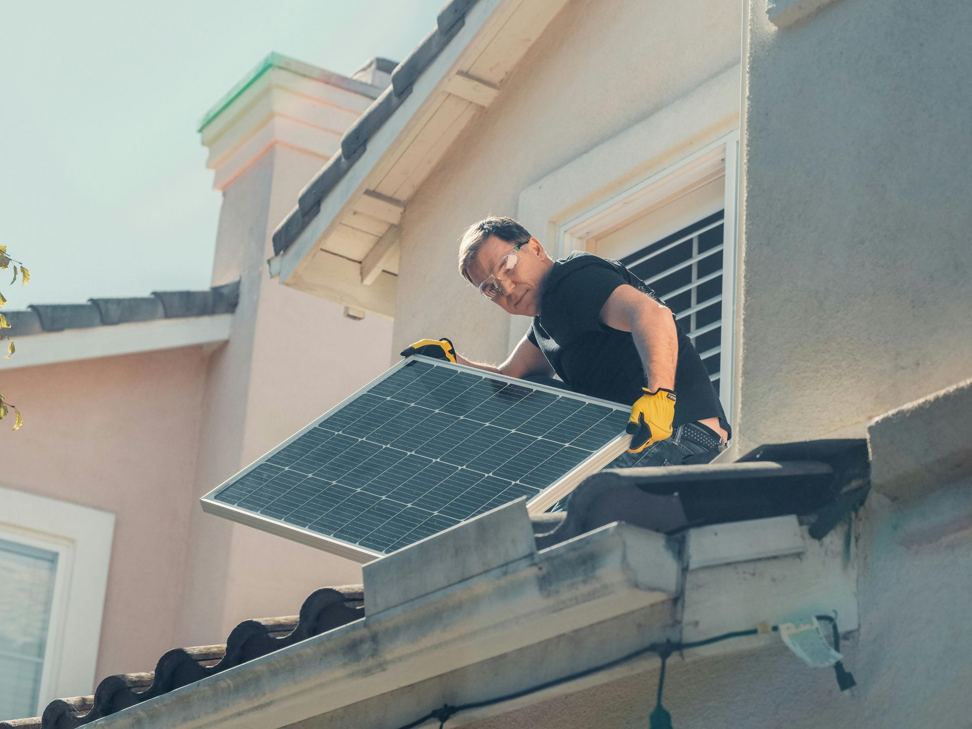 Solar Panel Installer On A Roof, Holding A Panel. Yellow Gloves, Sunny Day