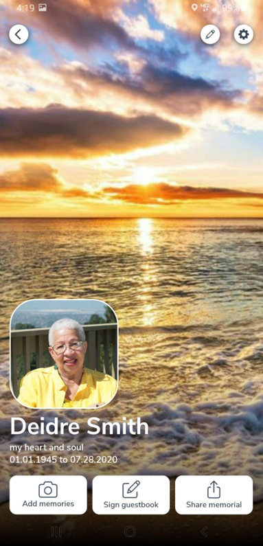A man in a yellow shirt is smiling in front of a sunset over the ocean.