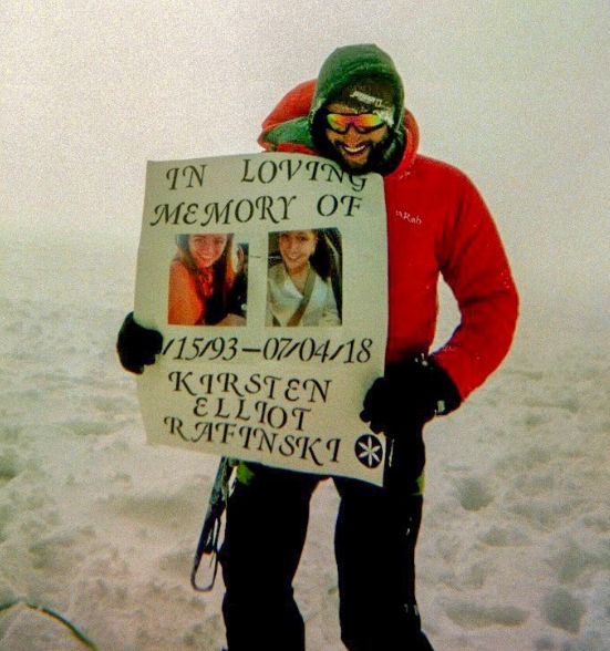 A man holding a sign that says in loving memory of kirsten elliot ratinski