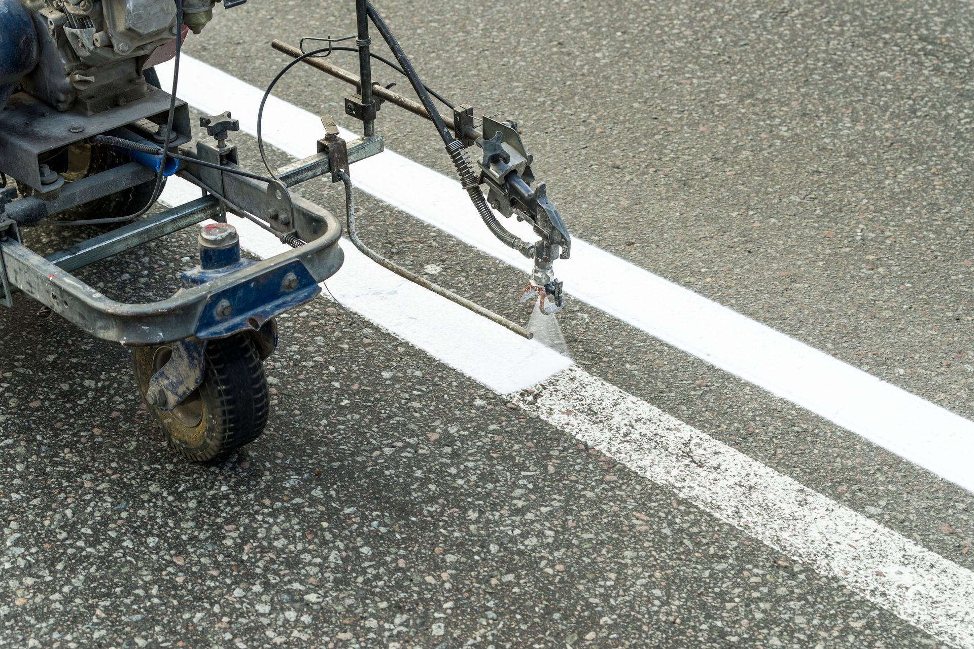 Close-up of a road marking machine painting white lane lines on asphalt.