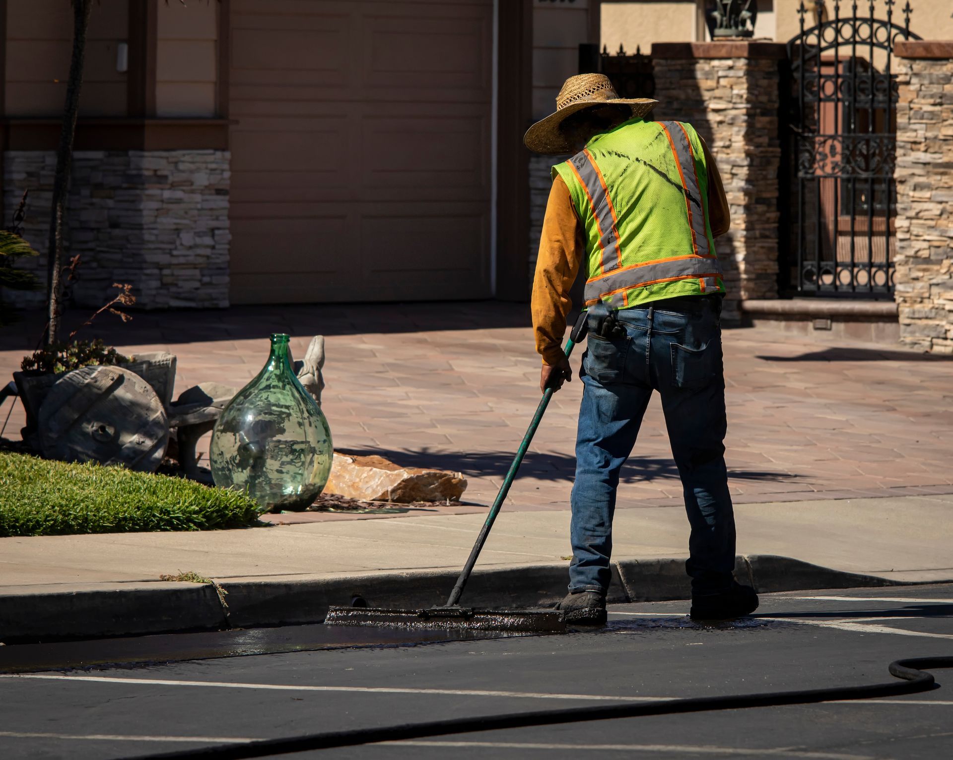 Worker in reflective vest using a hose to clean a street curb outside a house.