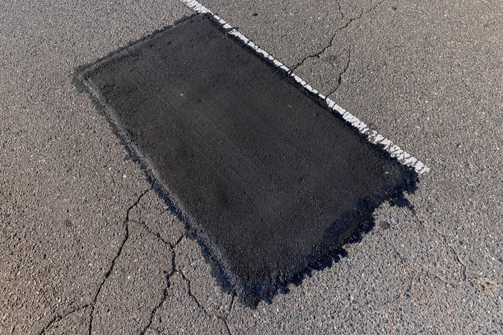 Black rectangular patch on cracked gray pavement, likely a repaired road section