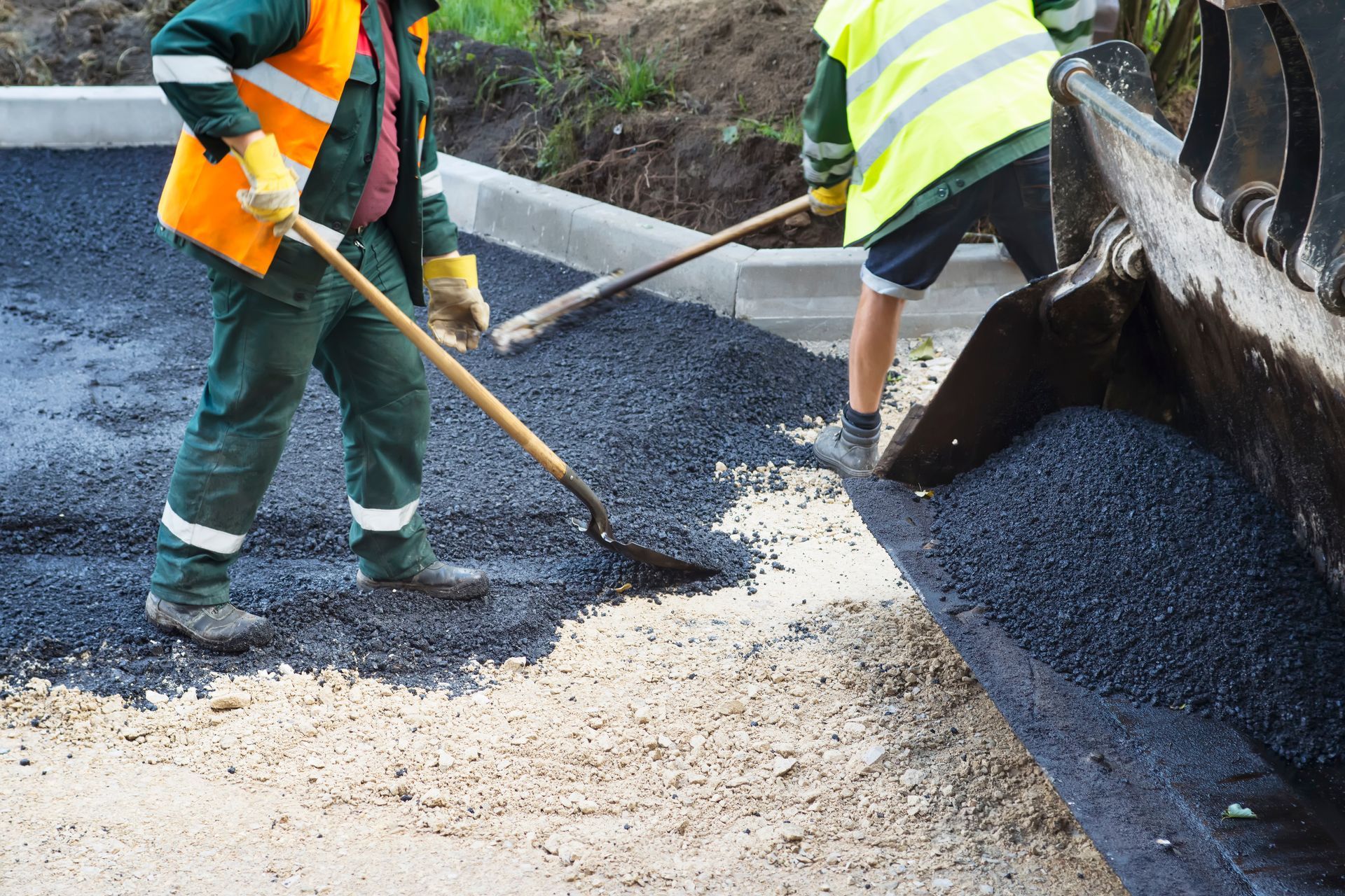 Road workers spreading fresh asphalt with shovels beside a paving machine