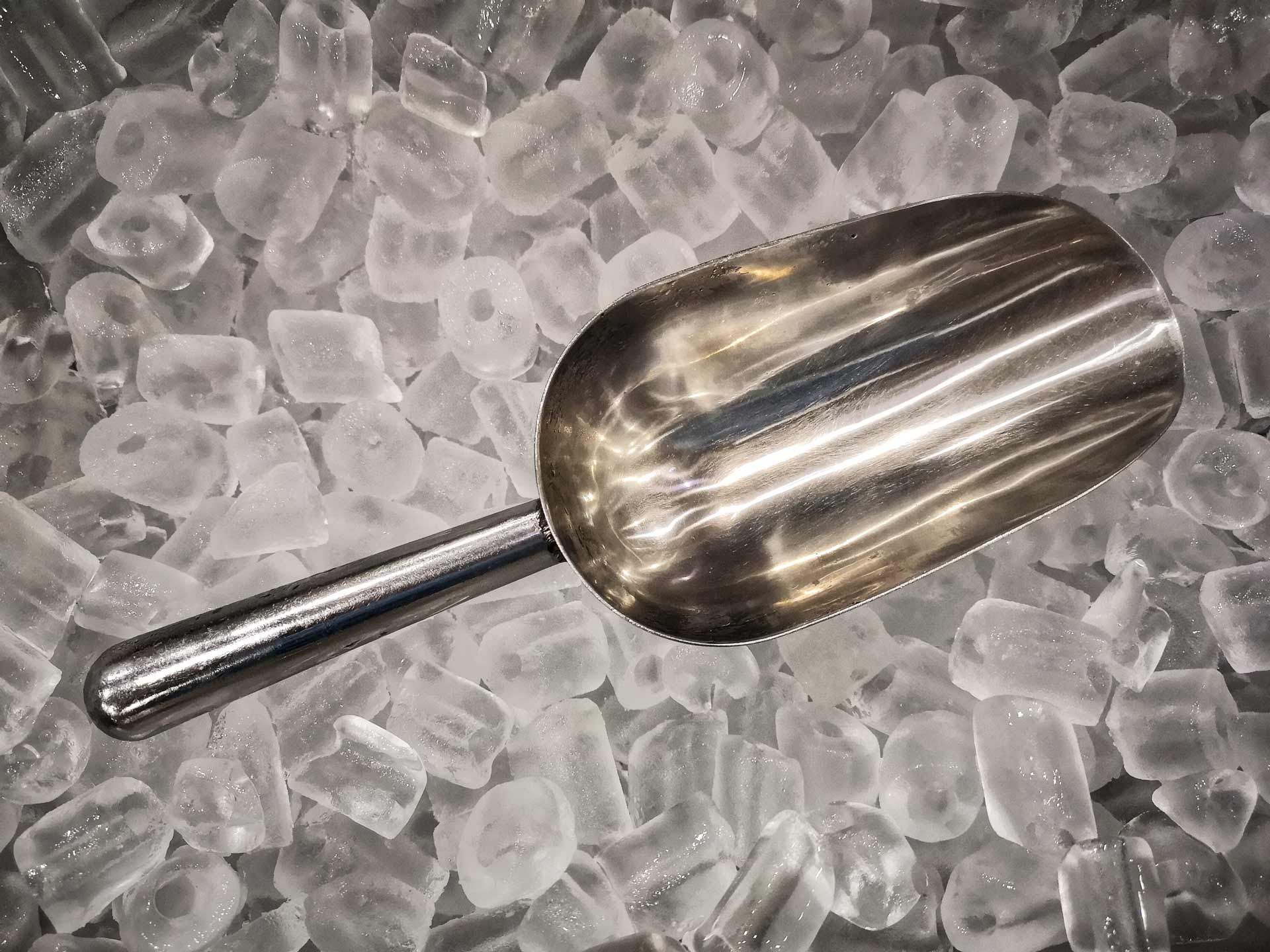 Metal ice scoop in a bin of ice cubes.