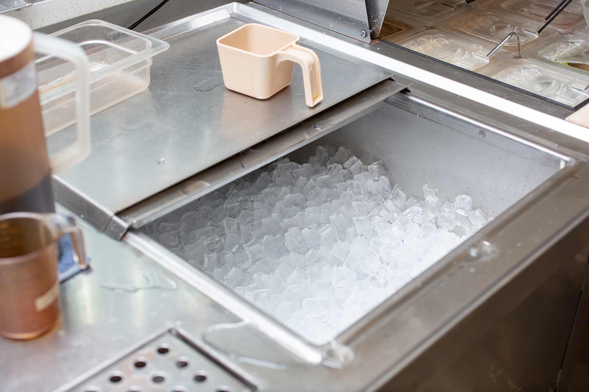 Commercial ice machine with open bin filled with ice. A water filtration system is mounted nearby.