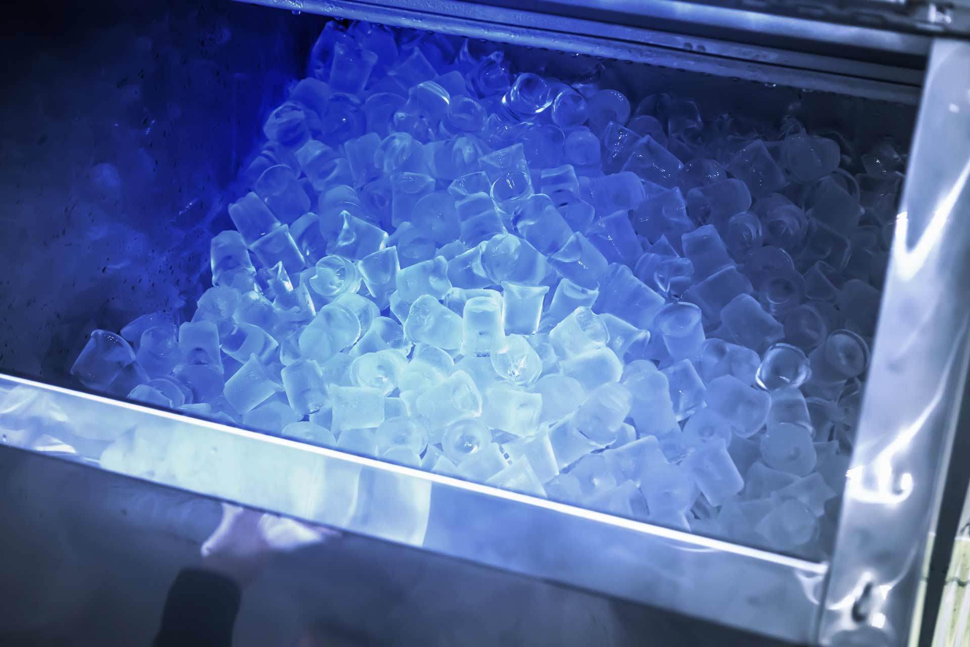 Ice machine filled with blue-tinted ice cubes. Shiny, stainless steel bin.