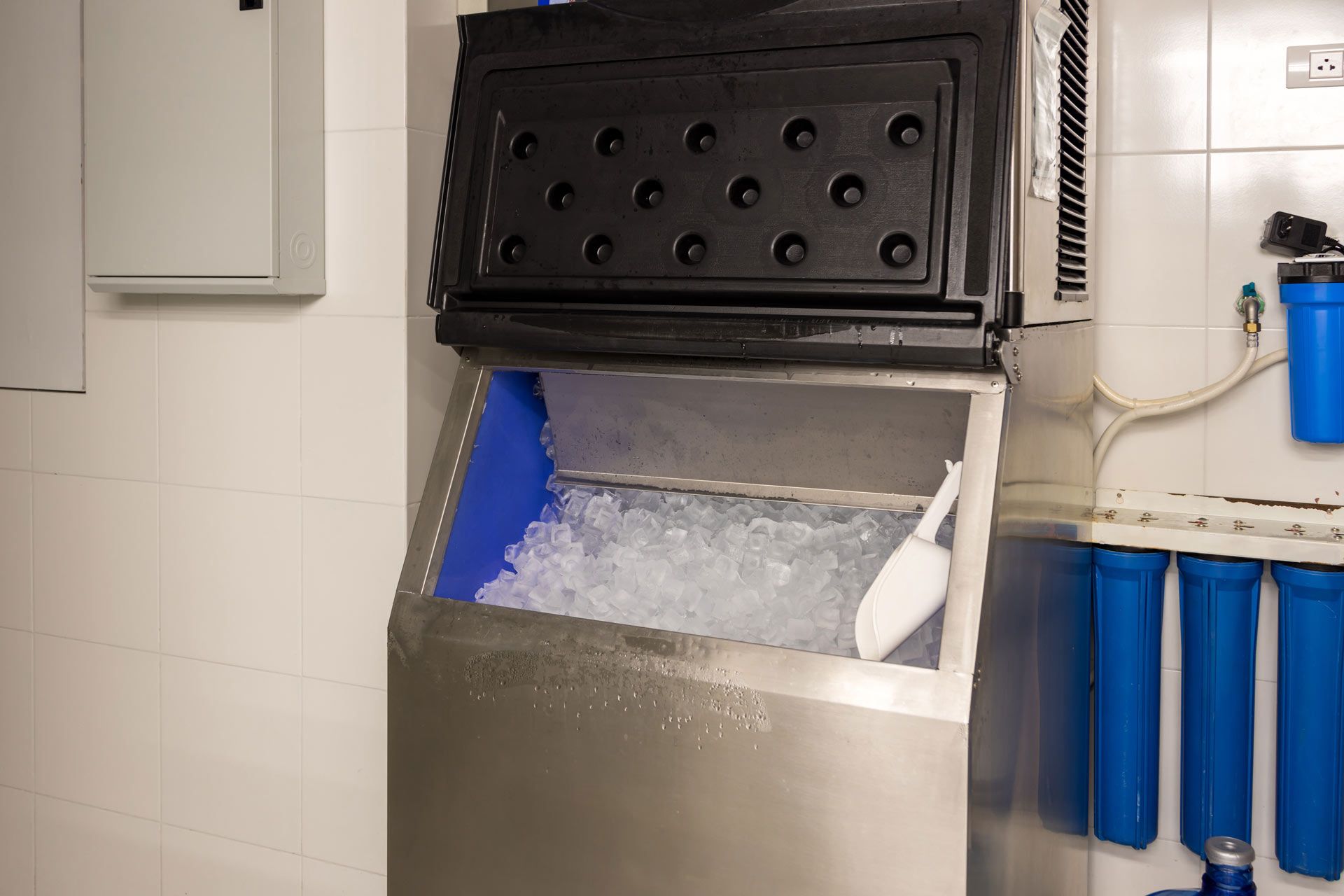 Ice machine with open bin filled with ice, white scoop inside.