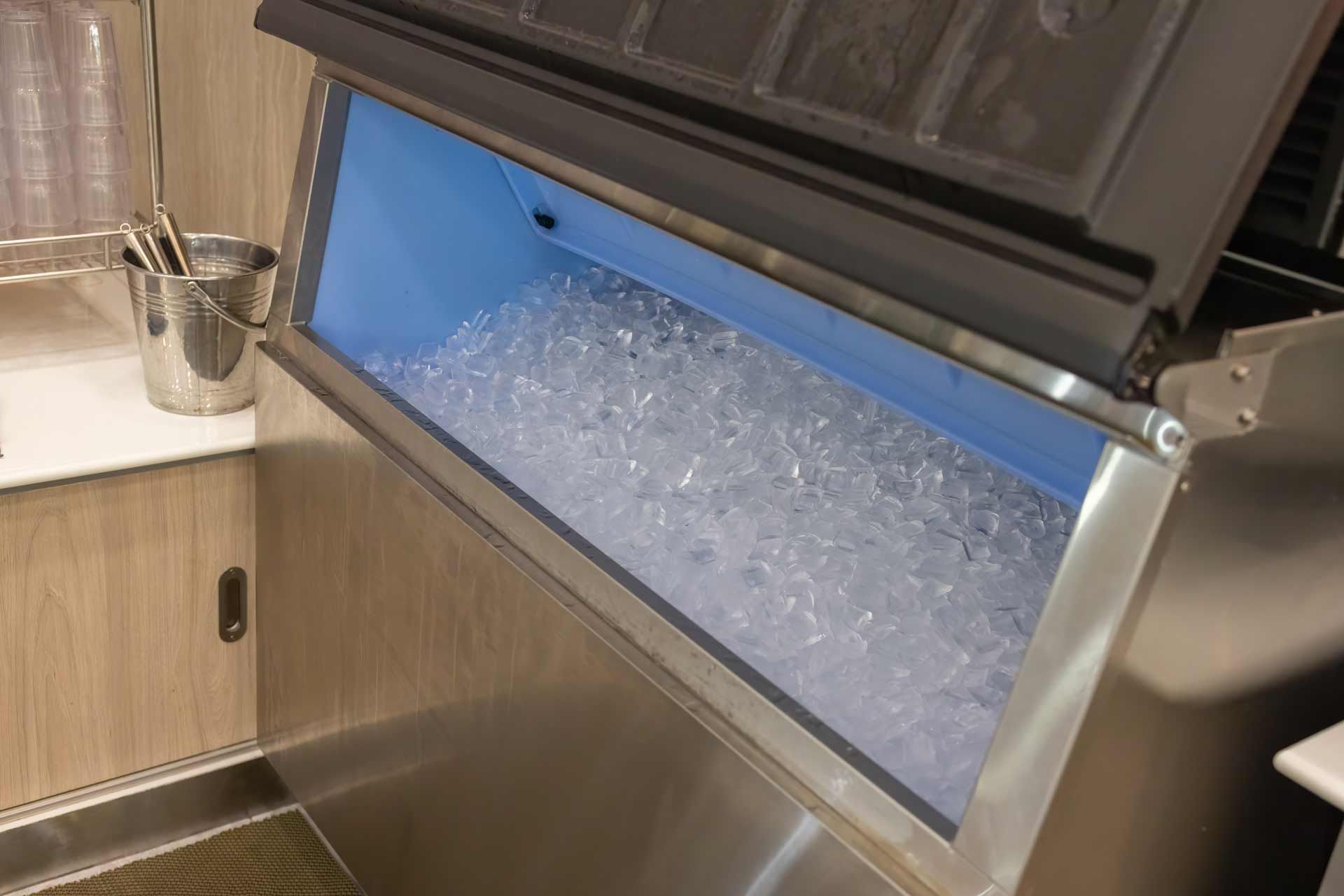Ice machine with an open lid, filled with ice cubes, in a restaurant setting.