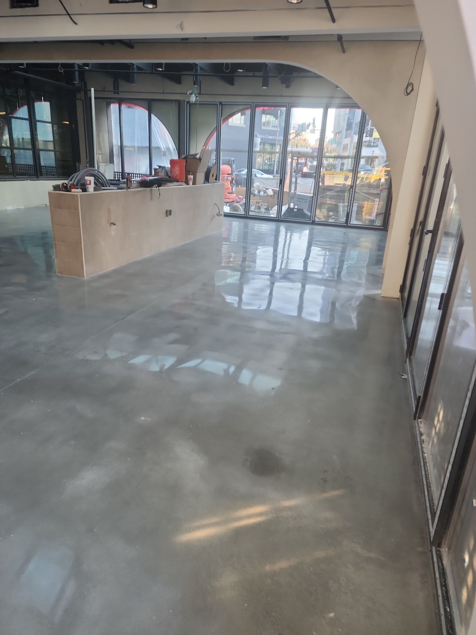 Empty lobby with polished concrete floor, reception desk, and large glass doors letting in daylight.