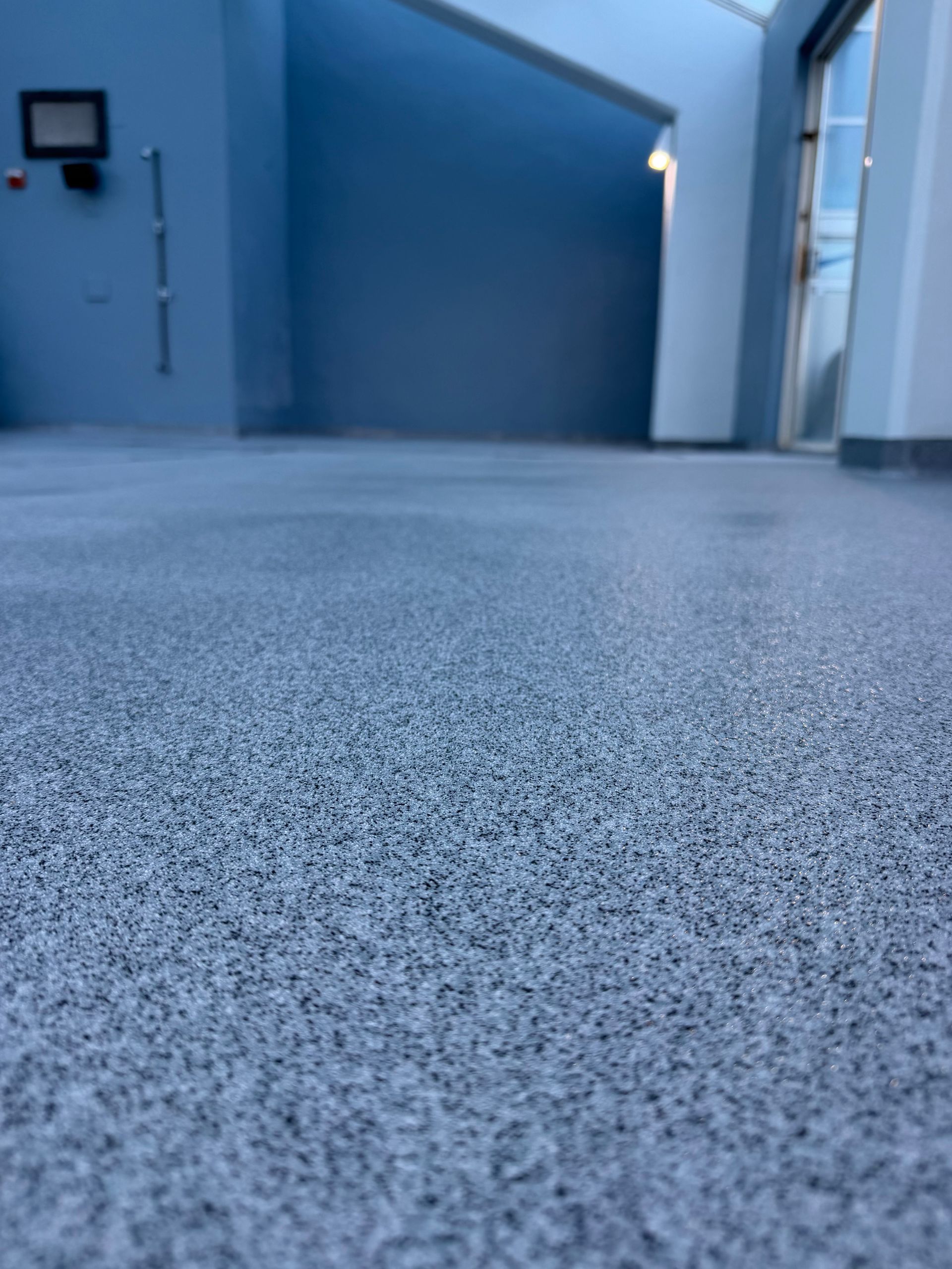 Blue-tinted hallway with a textured gray floor and windows on the right