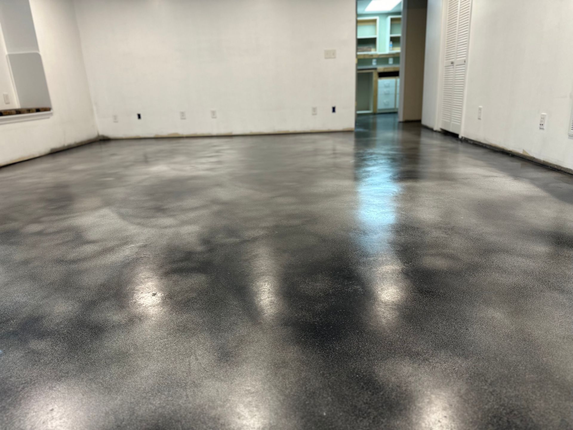 Empty room with glossy dark concrete floor and white walls, viewed from one end toward a doorway.